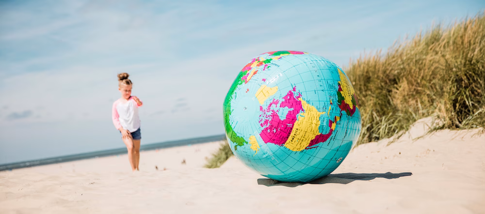 Pige leger på stranden med globus badebolden