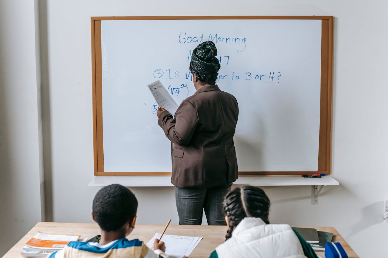 services-01 Teacher writing math lesson on whiteboard while students take notes in a classroom setting.